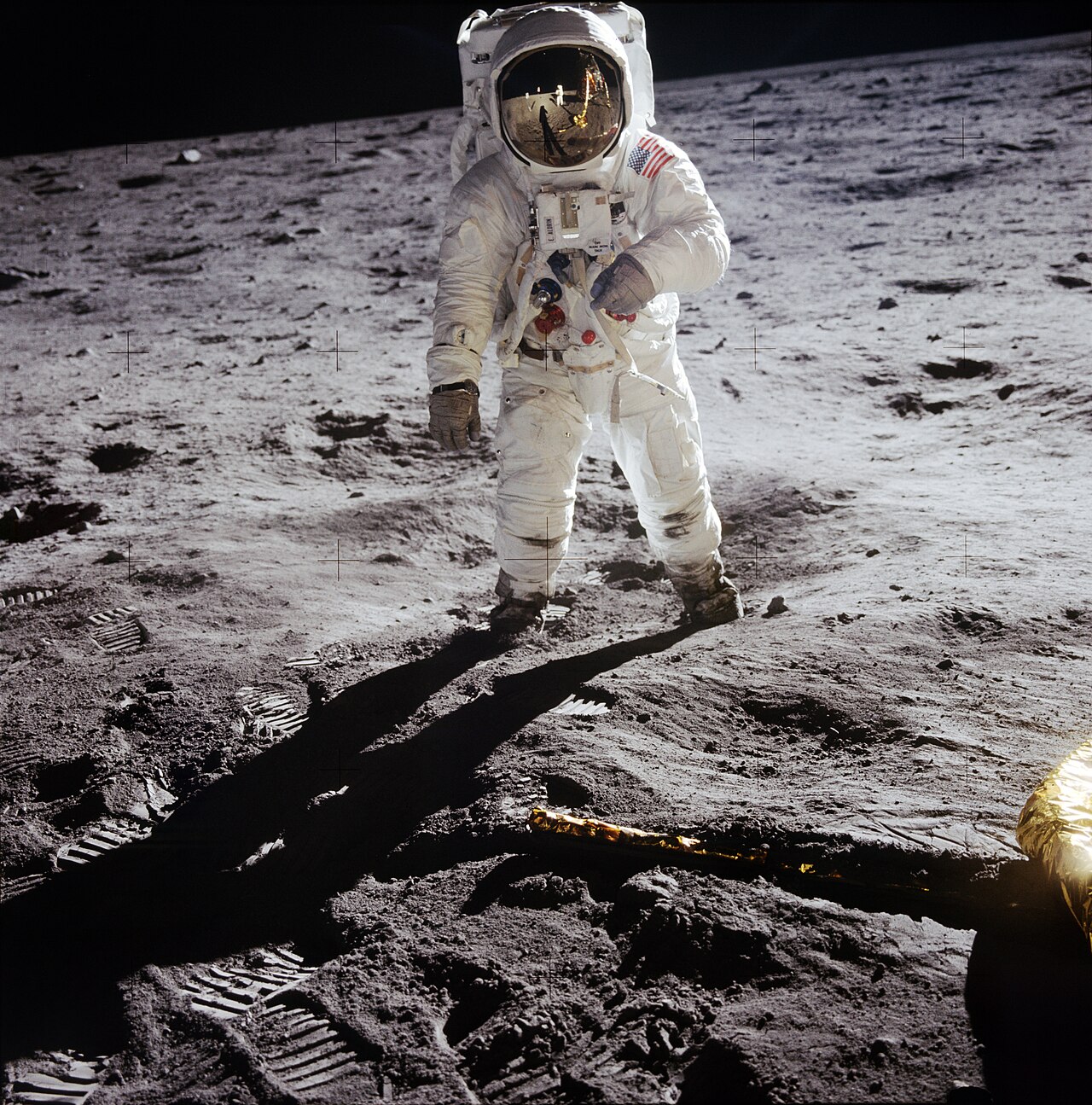 An astronaut stands on the moon wearing a shiny space suit.