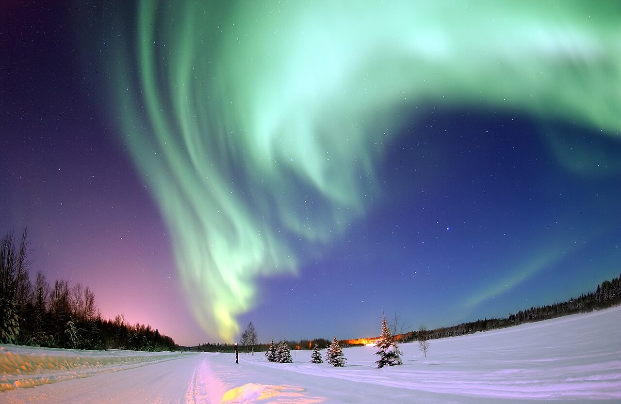 Green northern lights dance above a quiet lake in Alaska.