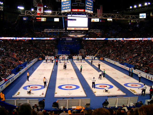 Curling players slide heavy stones down shiny lanes of ice.