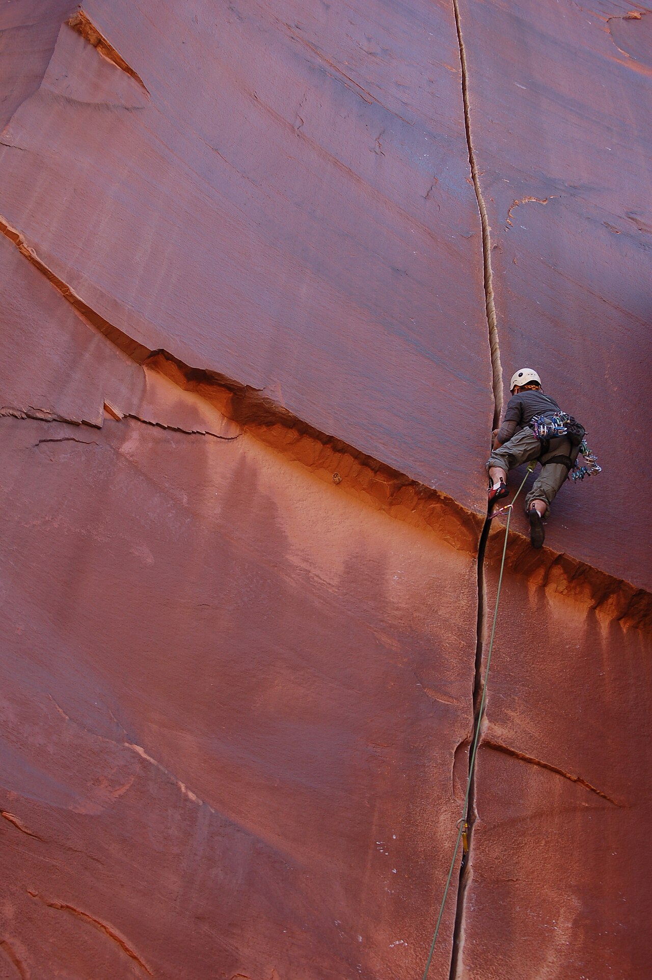 A climber grips tall red rock walls in the desert.